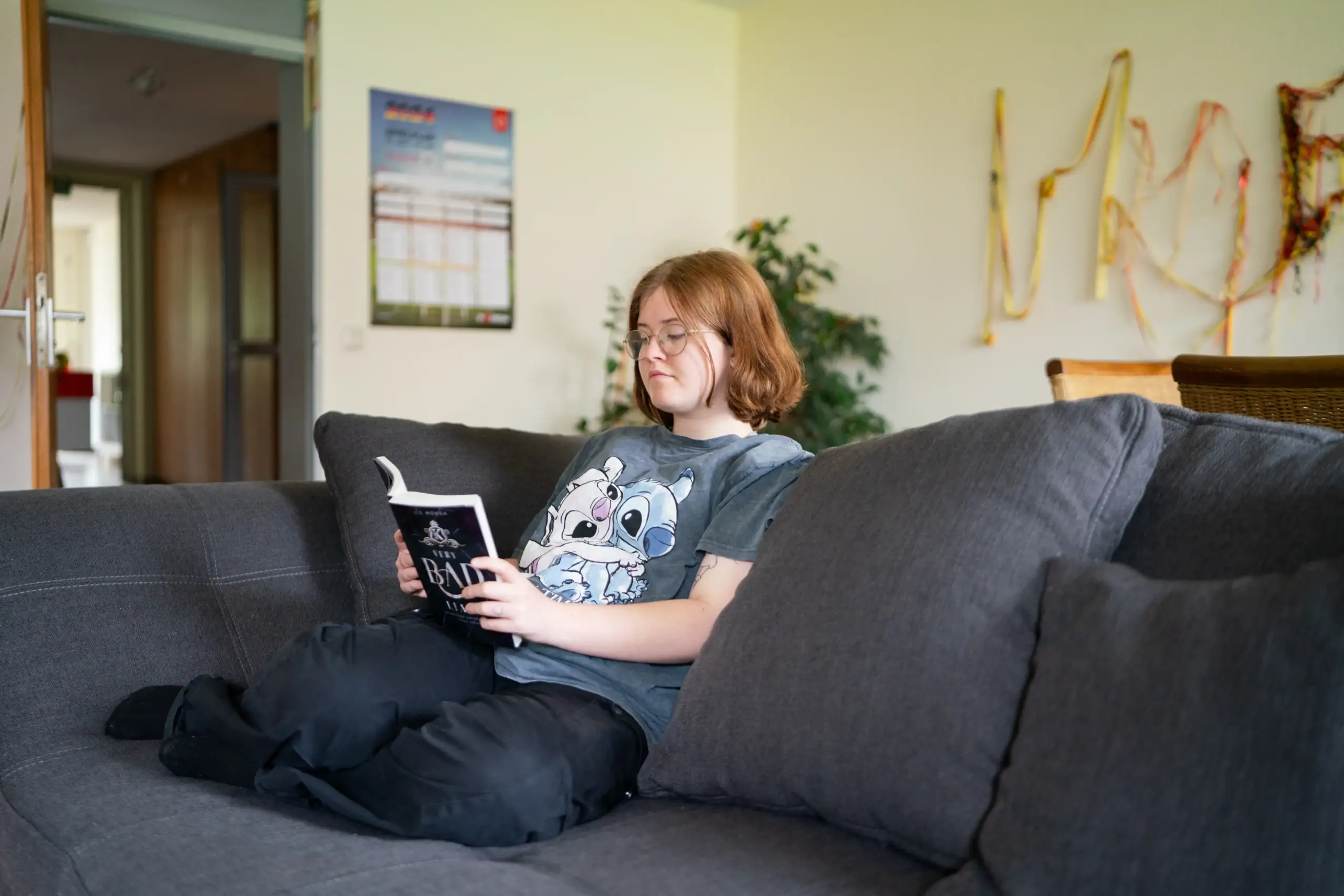Eine junge Frau sitzt auf einem Sofa und liest in einem Buch.