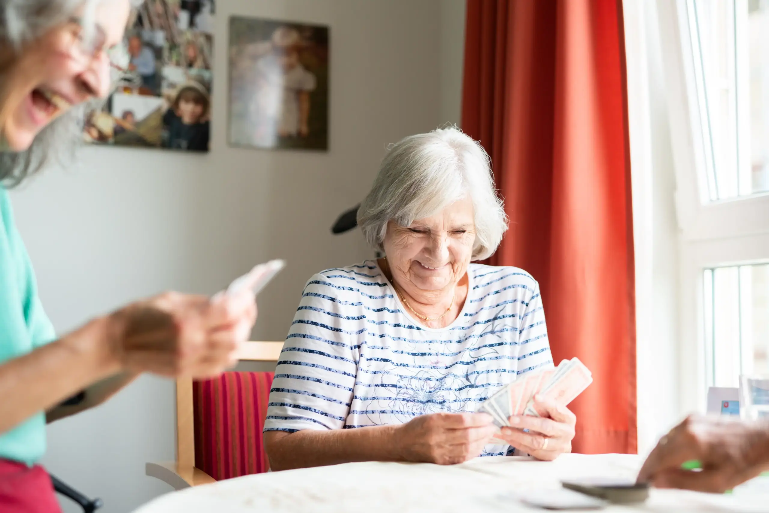 Zwei Frauen sitzen an einem Tisch und spielen Karten. Sie lachen herzlich.