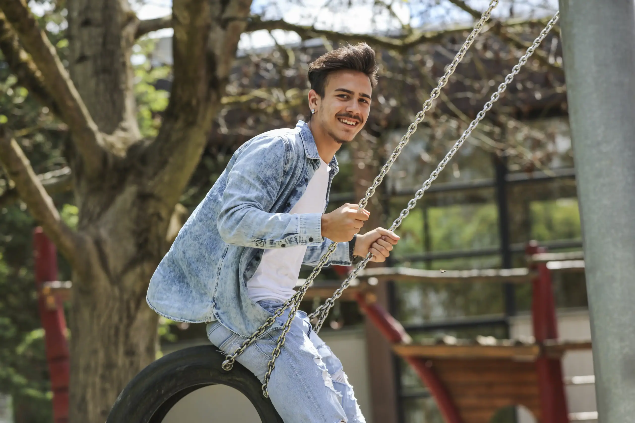 Ein Junge schaukelt auf einer Reifenschaukel. Er trägt eine Jeansjacke und lächelt in die Kamera.