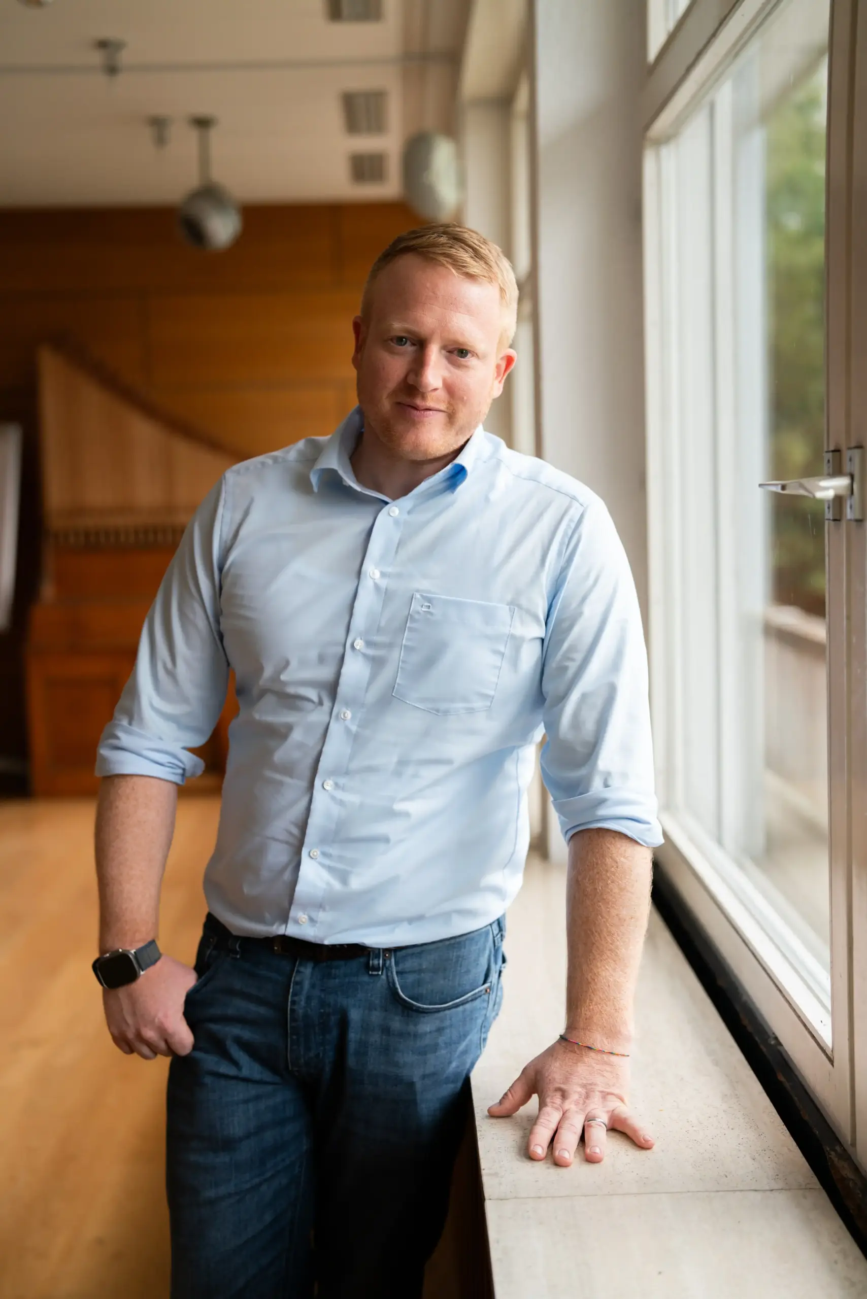 Christoph Röckinger lehnt an einem Fensterbrett. Er schaut in die Kamera und lächelt.