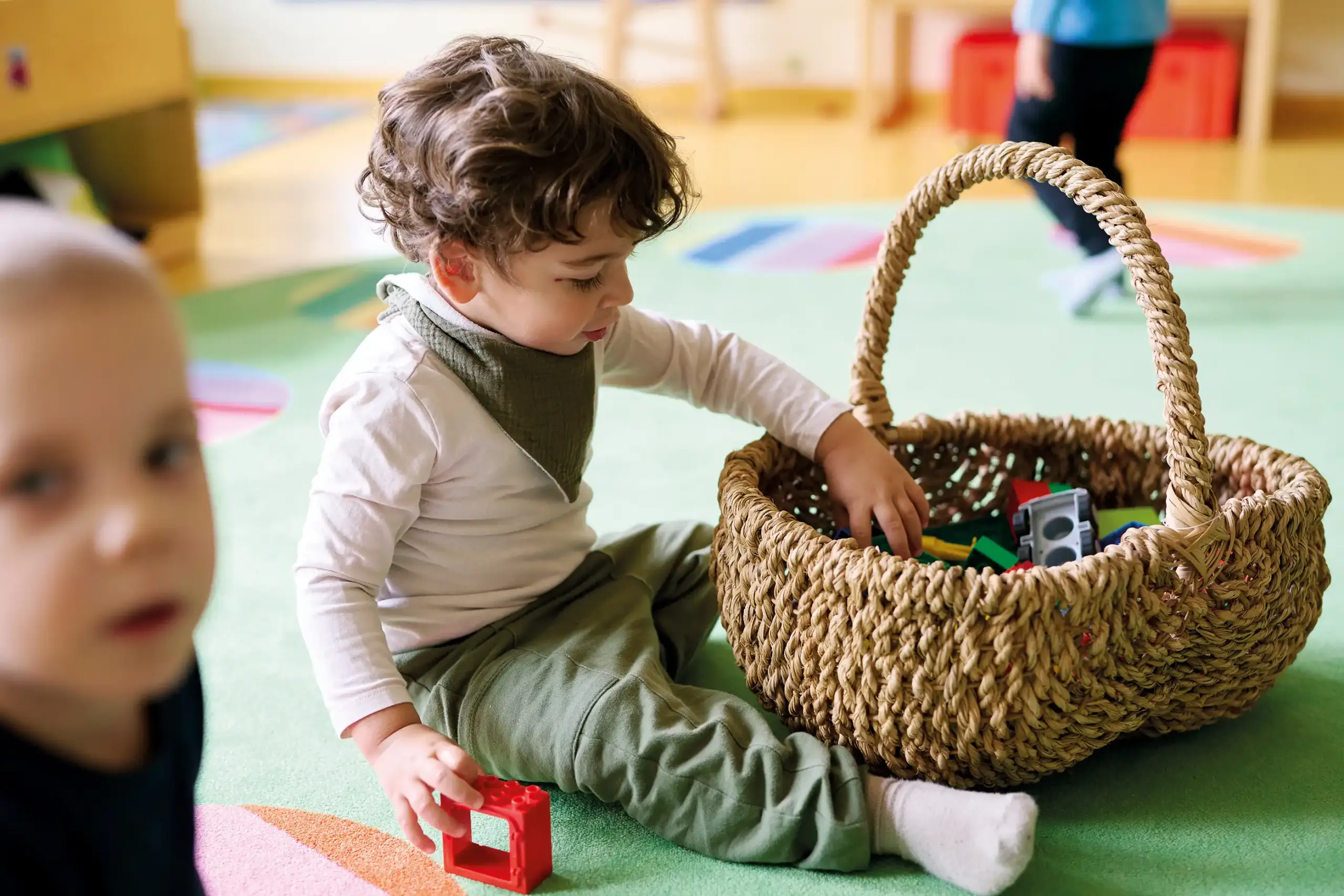 Ein Kind sitzt auf dem Boden und wühlt in einem Korb voller Duplo-Steine.