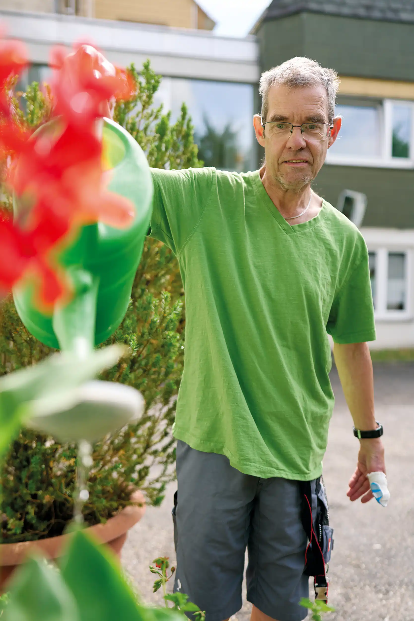 Ein Mann mit grünem T-Shirt gießt mit einer grünen Gießkanne Blumen.