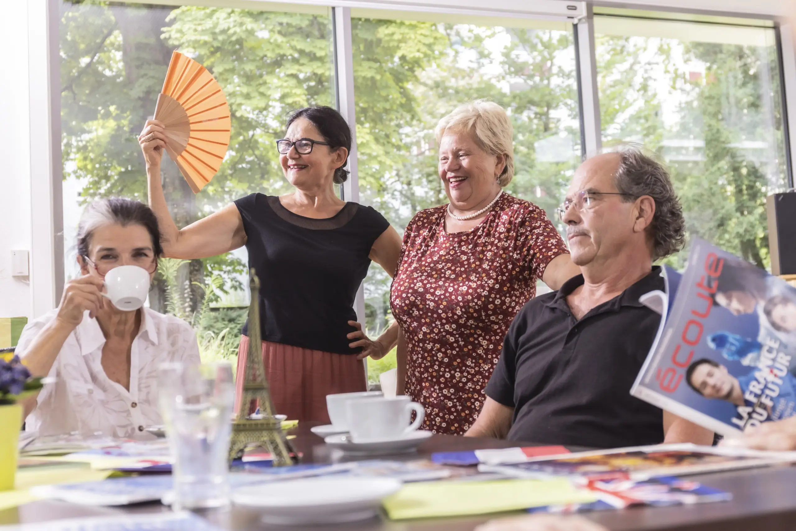 Quelle: BLV Zwei Personen sitzen an einem Tisch, zwei weitere stehen dahinter. Auf dem Tisch liegen Zeitschriften. Es stehen auch mehrere Kaffeetassen dabei.