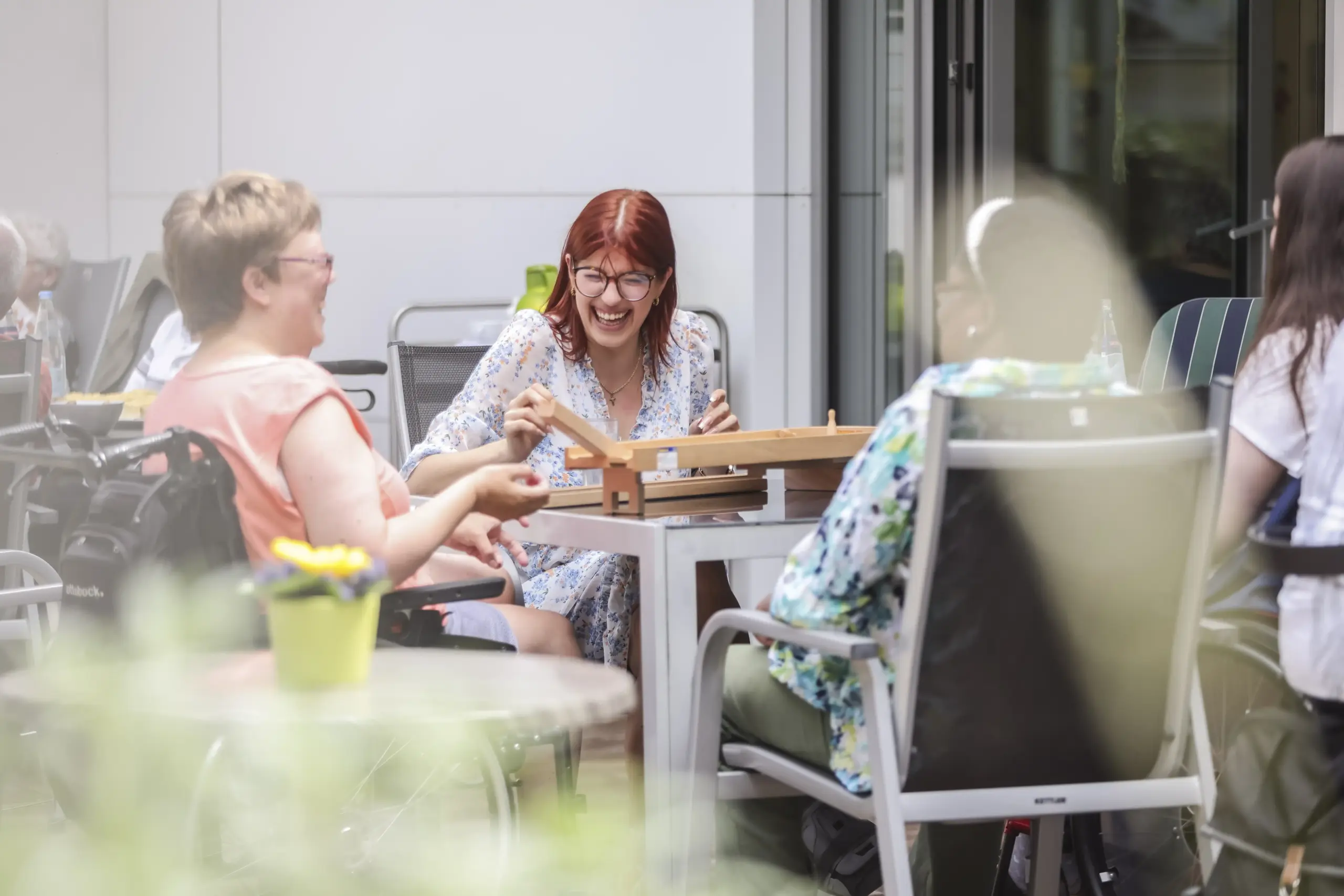 Vier Frauen sitzen an einem Tisch, eine davon sitzt in einem Rollstuhl. Sie lachen.