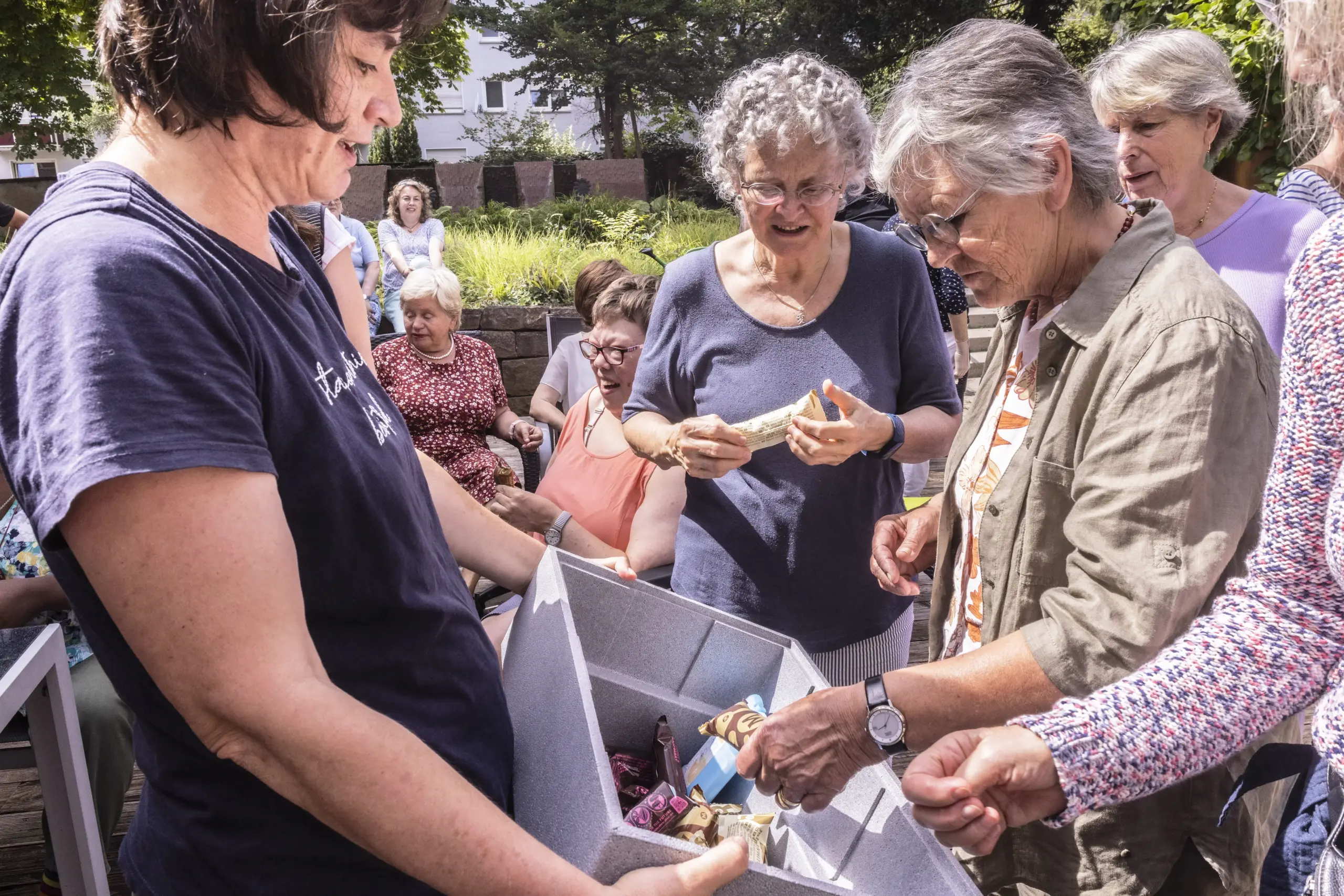 Quelle: BLV Quartiersmitarbeiterin Monika Scheytt teilt Eis an eine Gruppe älterer Frauen aus. Im Hintergrund sitzen weitere Personen auf Stühlen zusammen.