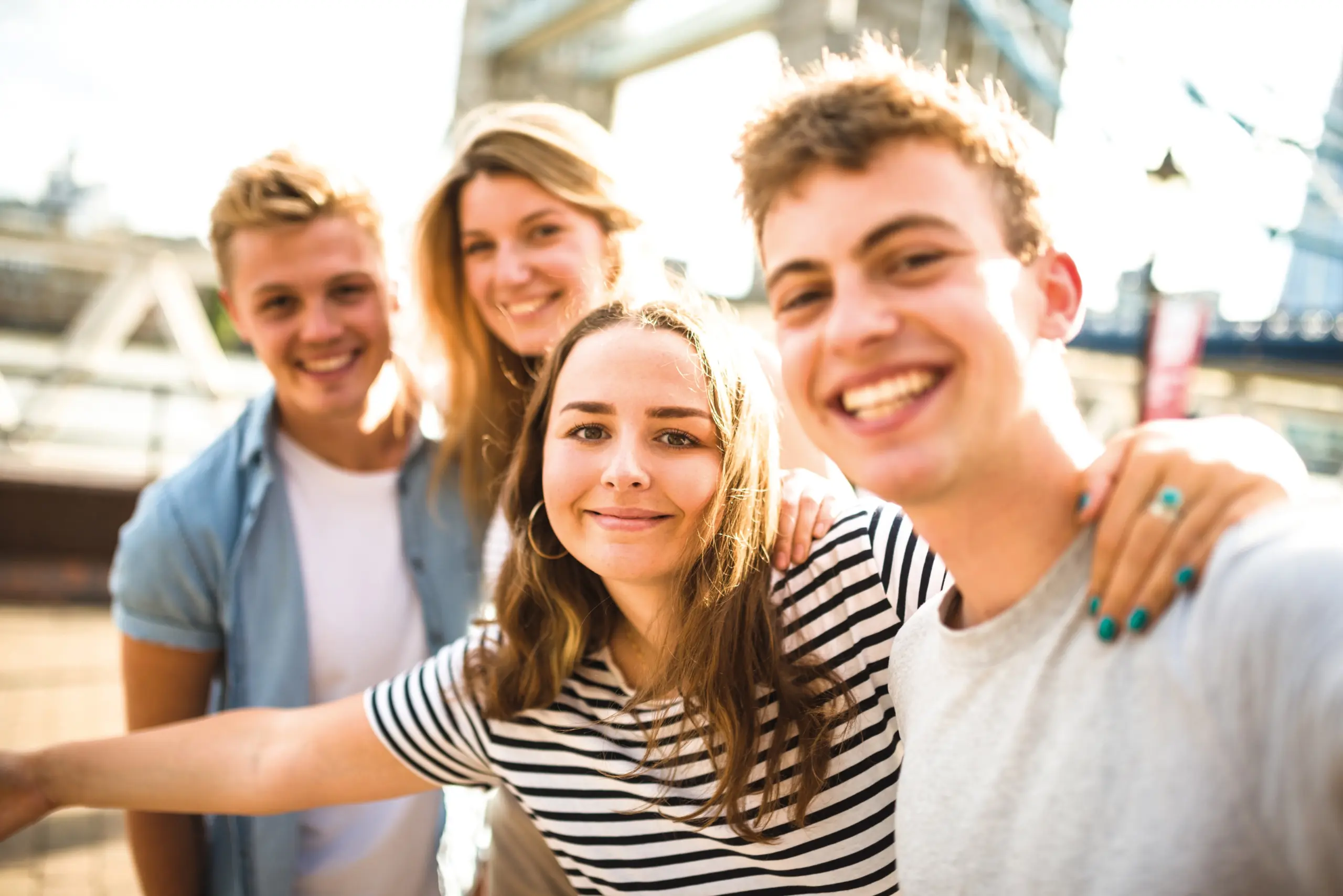 Vier junge Personen stehen nebeneinander und legen die Arme auf ihre Schultern. Sie lachen.