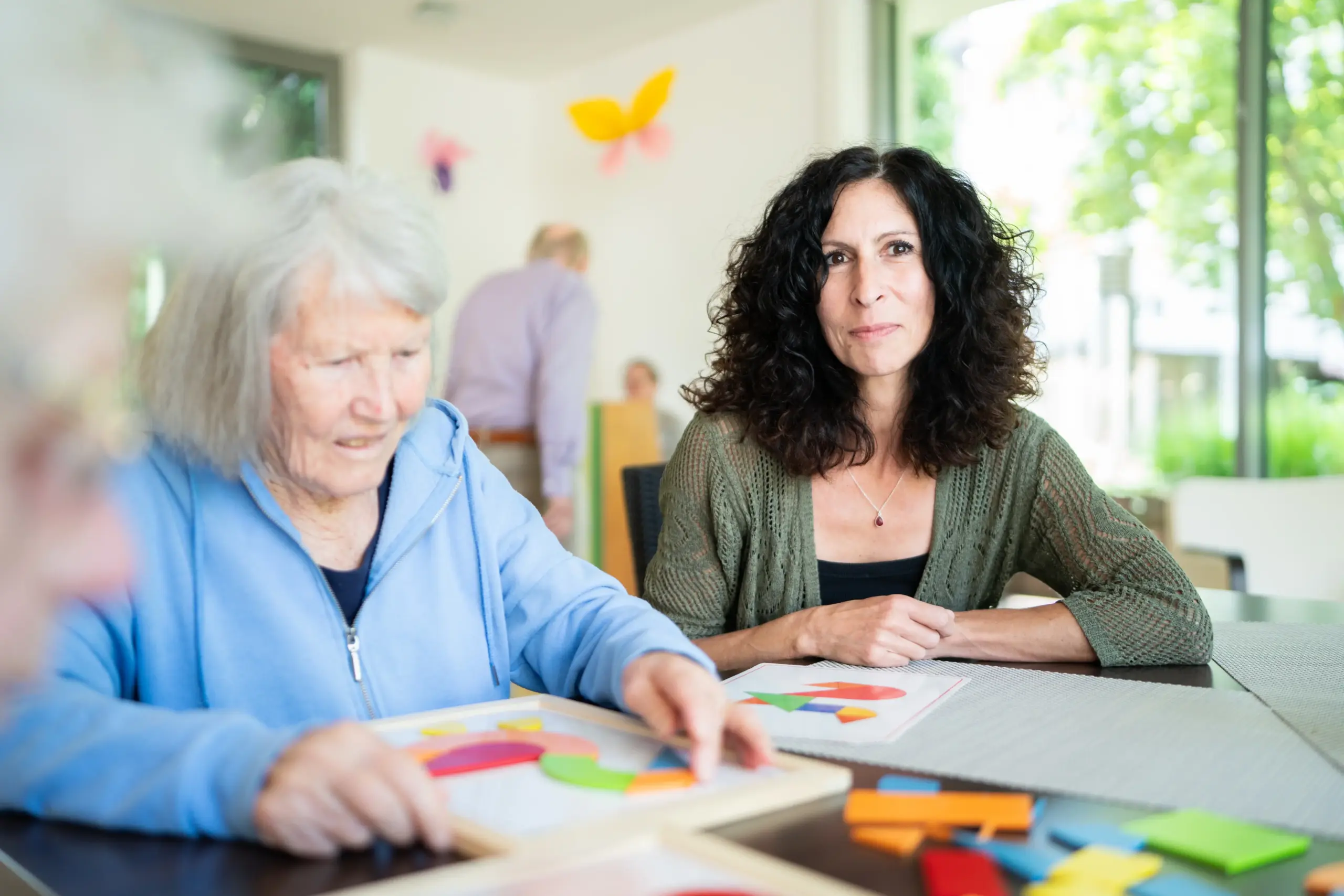 Zwei Frauen sitzen an einem Tisch und spielen ein Legespiel.