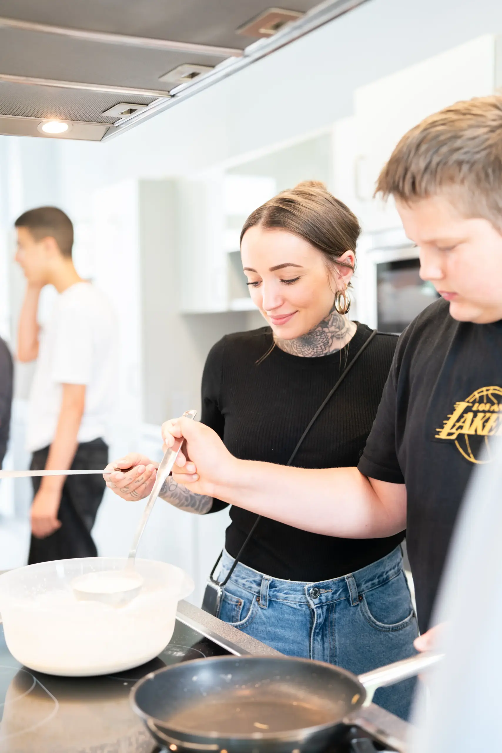 Eine junge Frau und ein Junge stehen zusammen am Herd. Der junge schöpft Teig aus einer Schüssel in eine Pfanne.