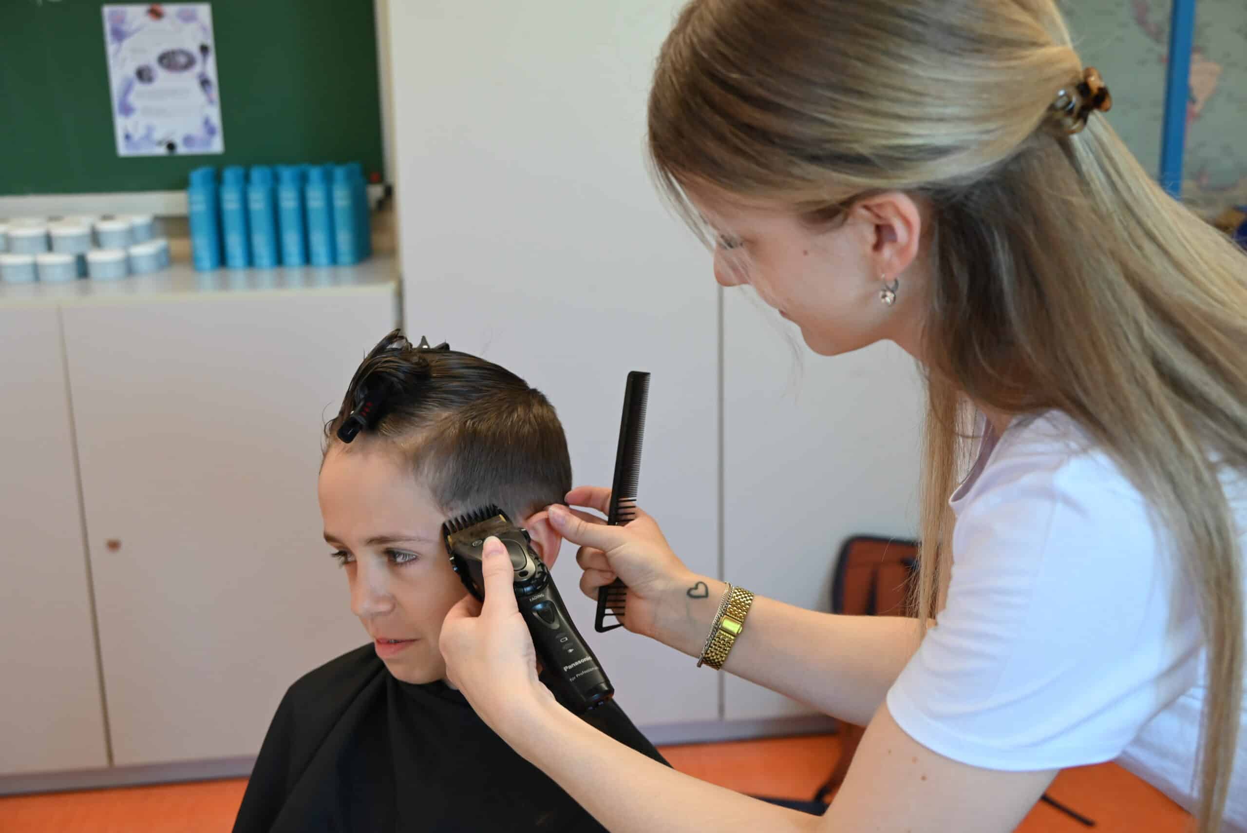 Ein kleiner Junge bekommt von einer Frau mit einem Rasierapparat die Haare geschnitten.