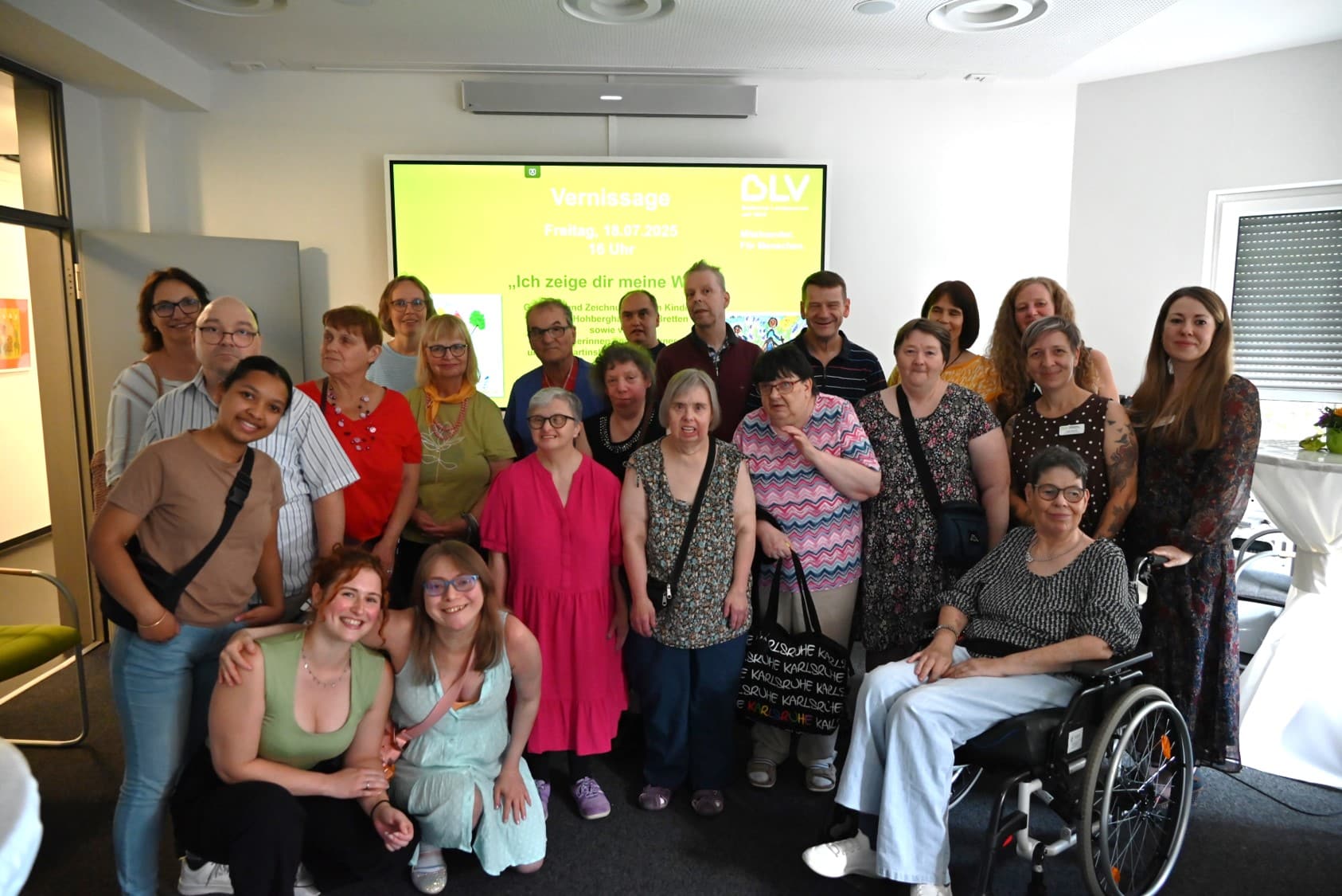 Gruppenbild der Künstlerinnen und Künstler aus dem Martinshaus. Eine der Personen sitzt im Rollstuhl. Alle lachen in die Kamera. Mit dabei sind auch einige Betreuerinnen und Betreuer sowie Evelyn Schmidt (Einrichtungsleitung Martinshaus, ganz rechts) und Julia Scherf (Leitung Hohbergschule, zweite von rechts).