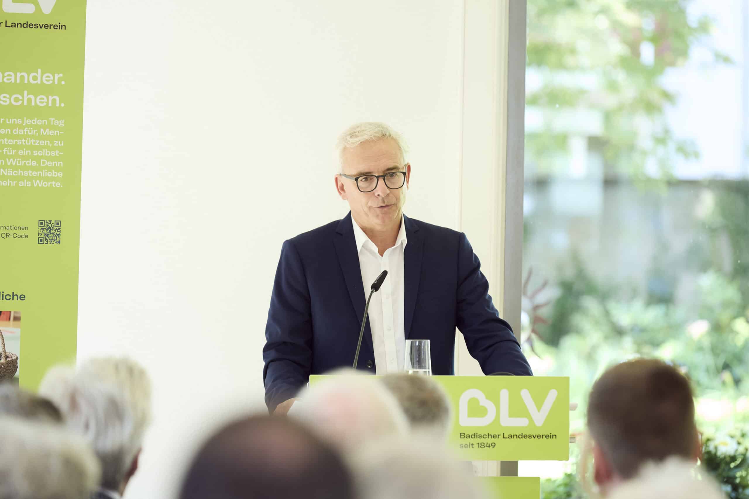 Landrat Dr. Christoph Schnaudigel steht an einem Pult und hält eine Rede. Er trägt einen dunkelblauen Anzug und ein weißes Hemd.