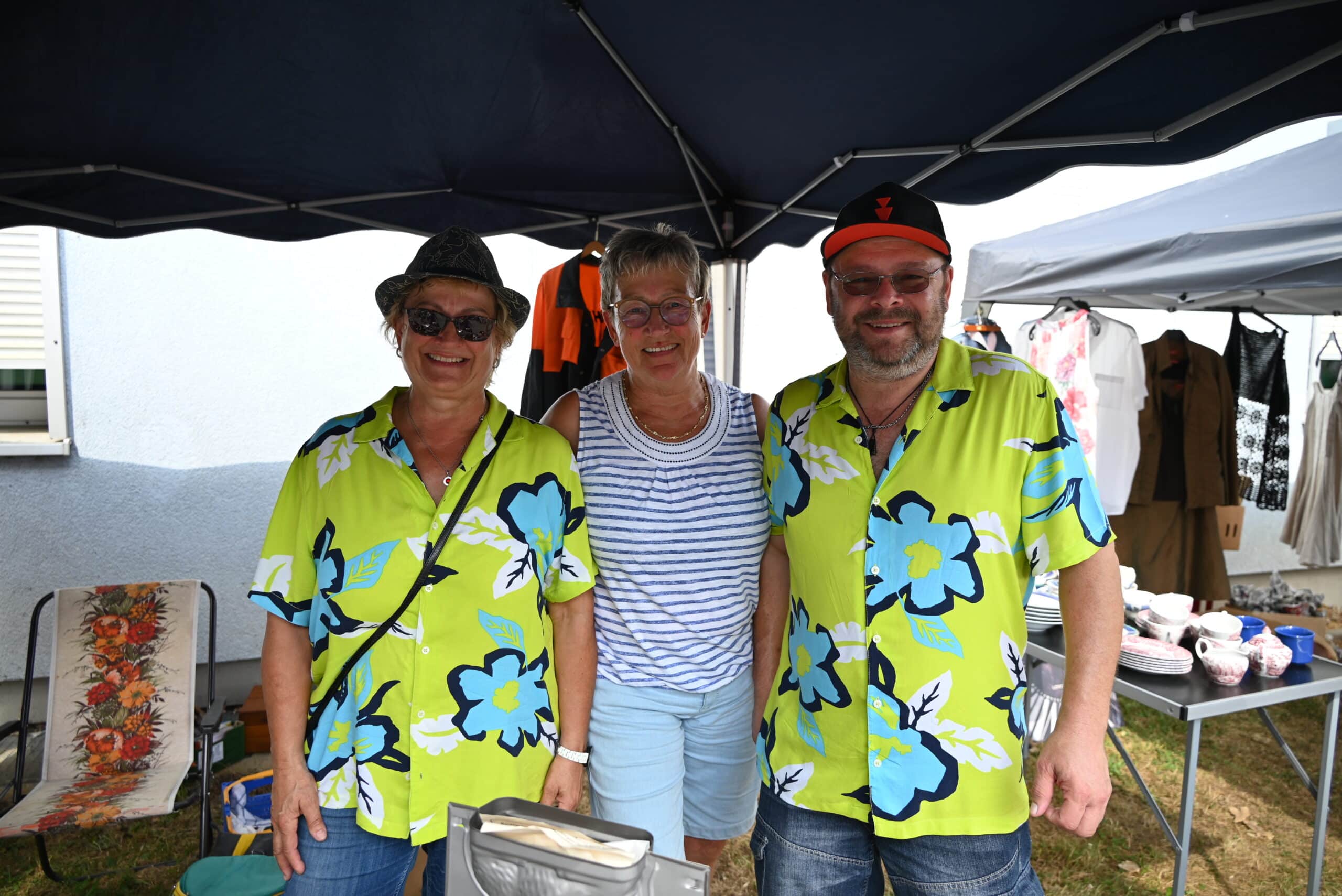 Quelle: BLV Drei Personen stehen unter einem dunkelblauen Pavillon. Zwei Personen tragen ein hellgrünes Hawaii-Hemd mit großen hellblauen Blüte darauf.