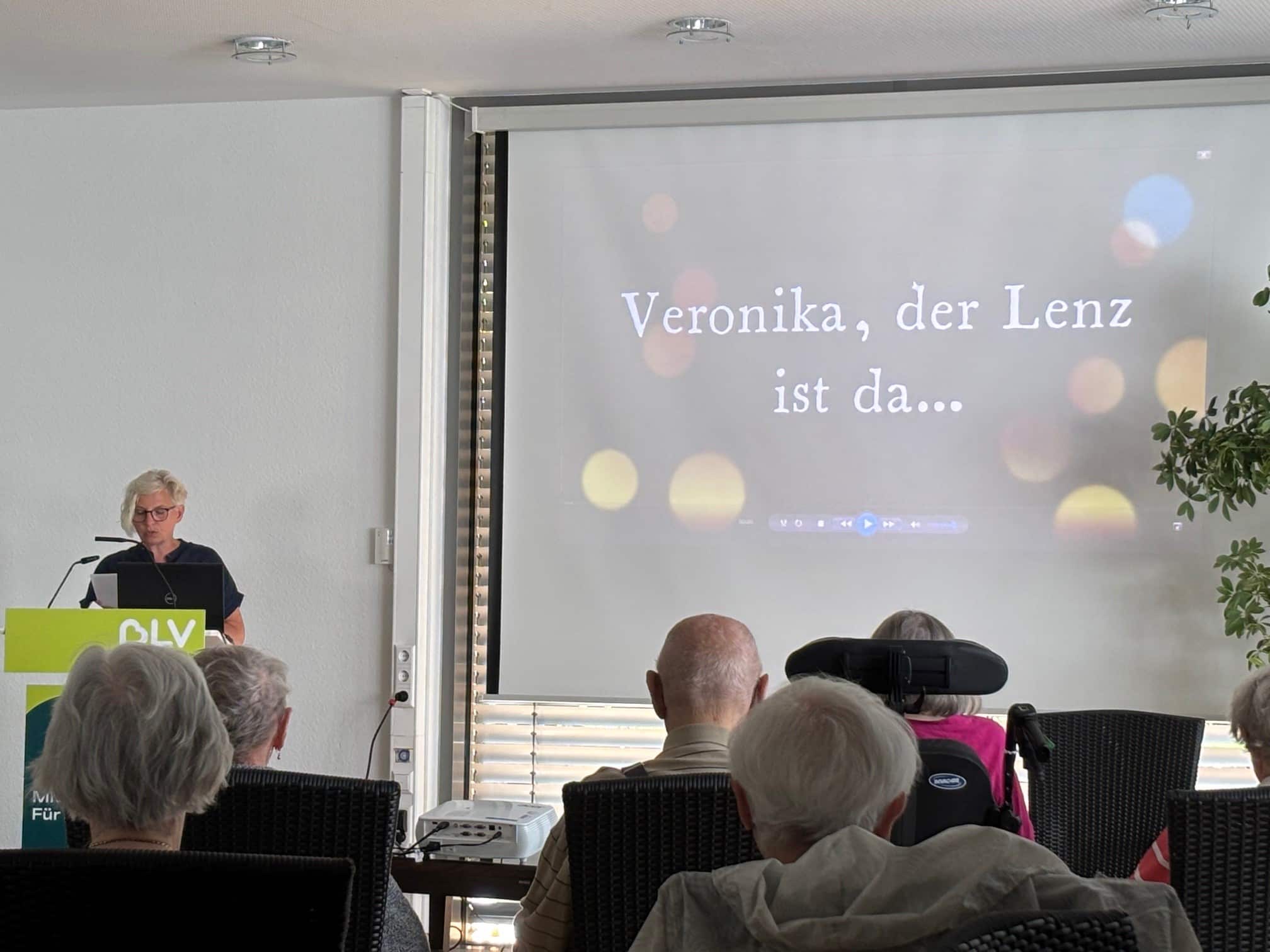 Quelle: BLV Frau Kammerer steht an einem Pult und spricht. Neben ihr wird mit einem Beamer eine Präsentation auf eine Leinwand gestrahlt. Mehrere Menschen sitzen im Publikum und hören zu.