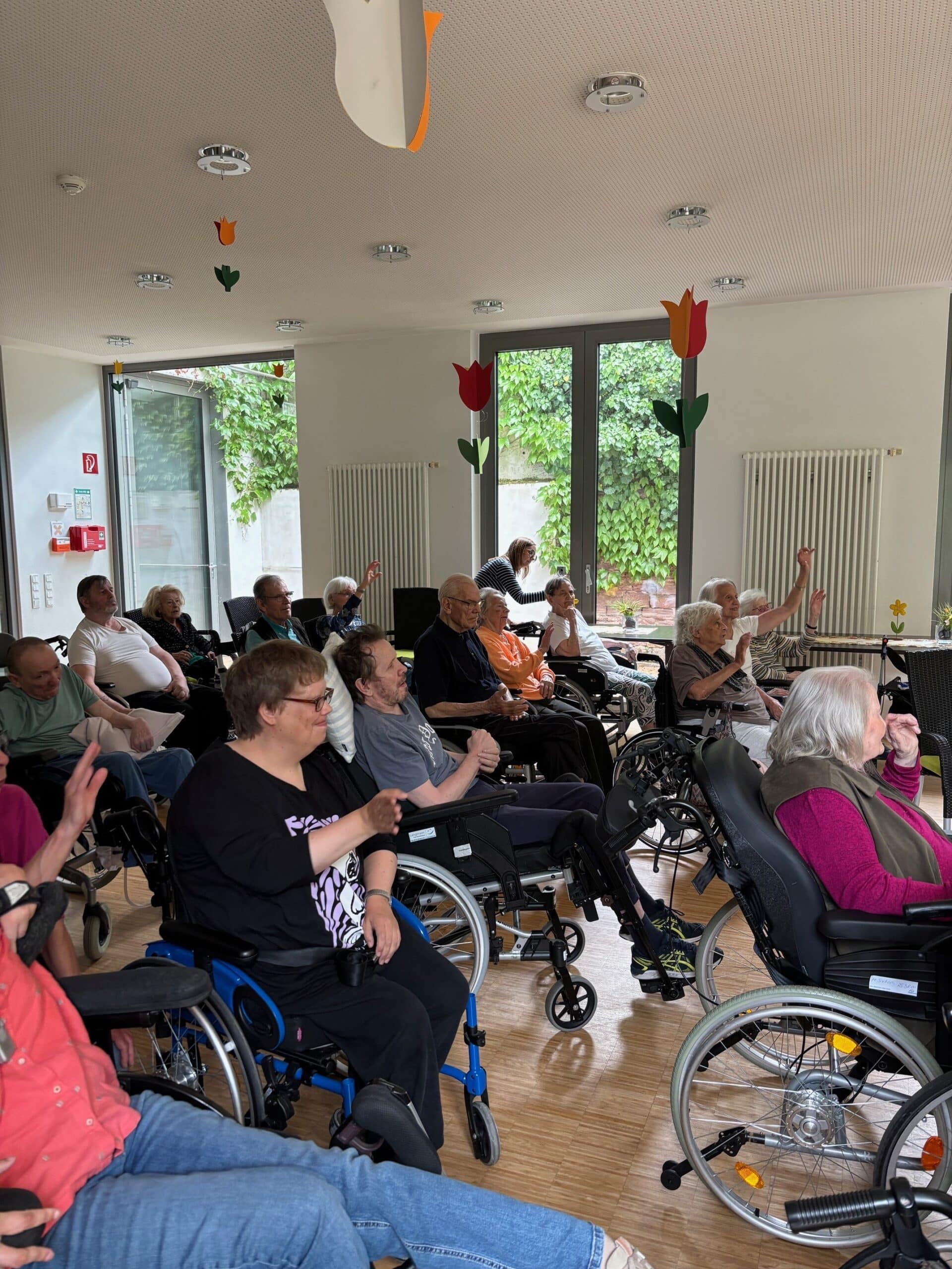 Quelle: BLV Viele ältere und jüngere Menschen sitzen nebeneinander im Publikum. Die meisten sitzen im Rollstuhl. Sie singen und klatschen.