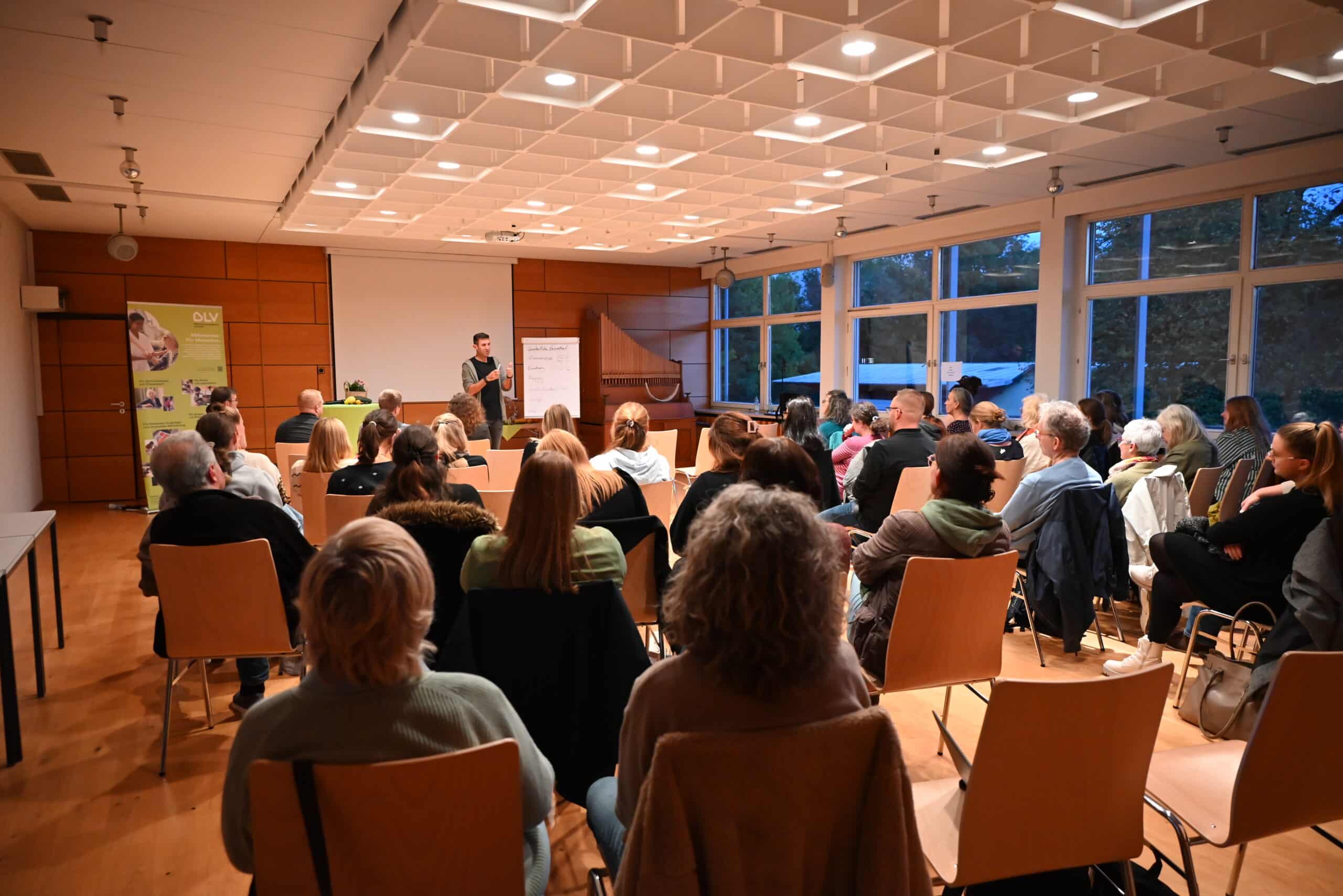 Quelle: BLV Viele Menschen, jung und alt, sitzen auf Holzstühlen und hören einem Vortrag im Hohberghaus zu.