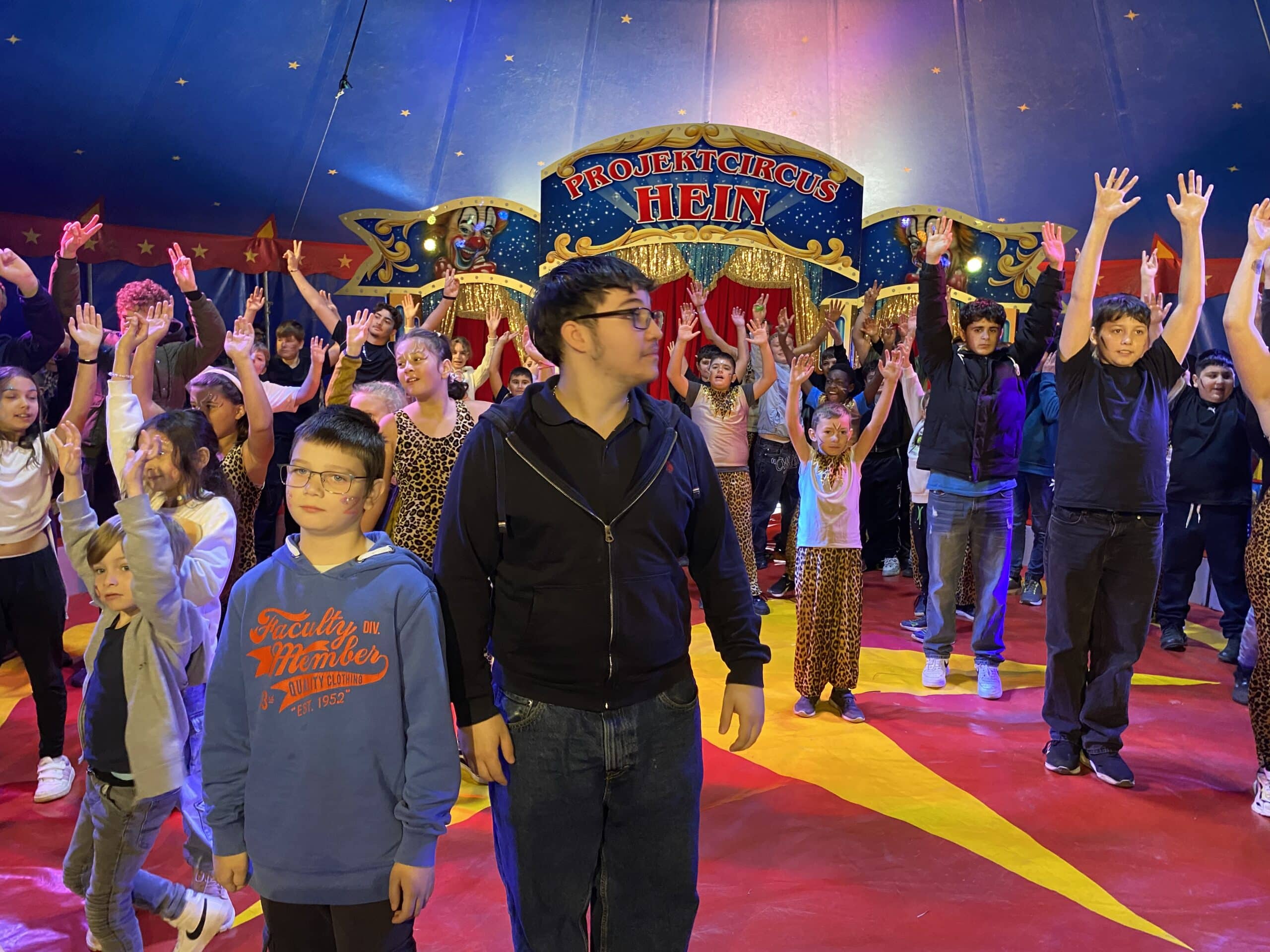 Quelle: BLV Viele Kinder stehen in der Manege eines Zirkuszelts. Sie lachen und werfen die Arme nach oben.