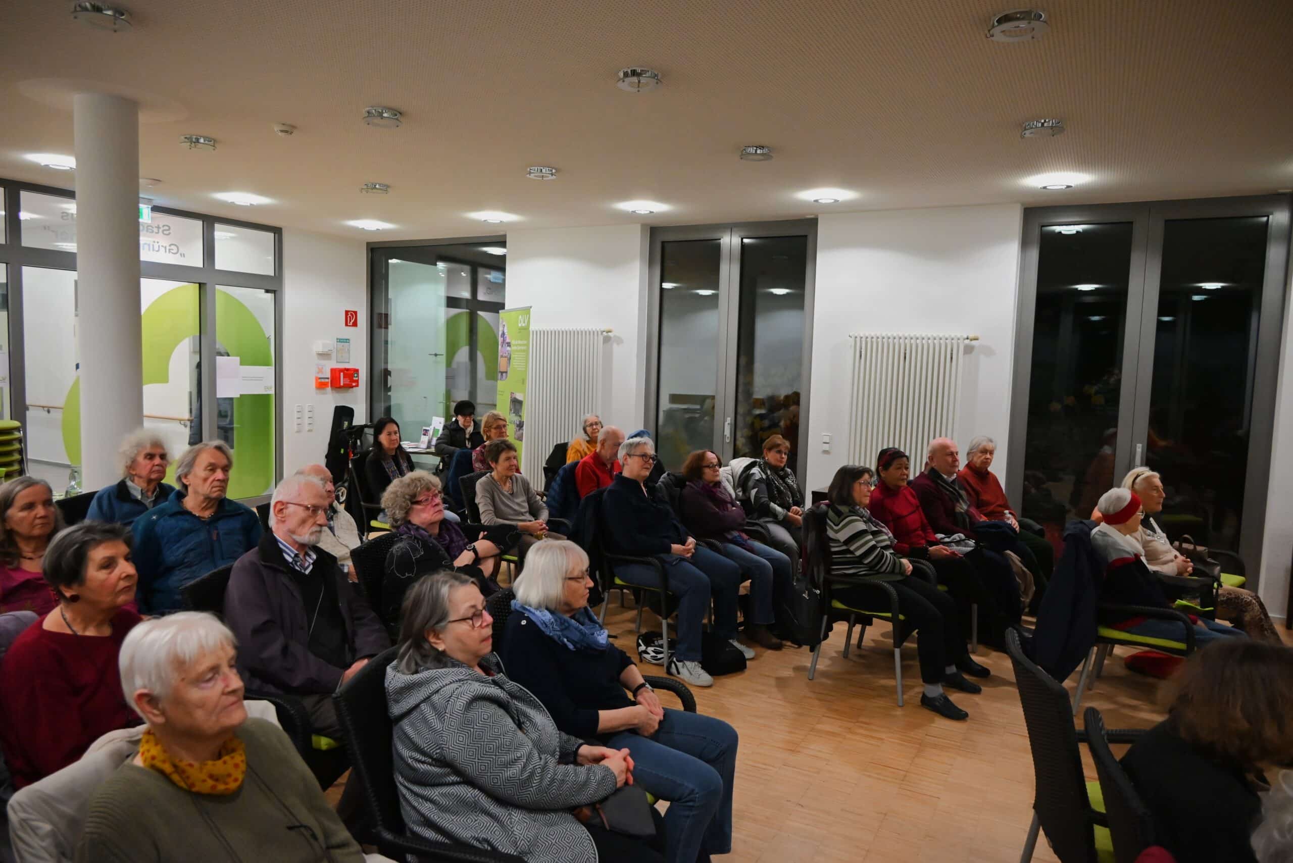 Eine Gruppe Menschen sitzt auf Stühlen in einem Veranstaltungsraum und wartet auf den Beginn des Filmes.
