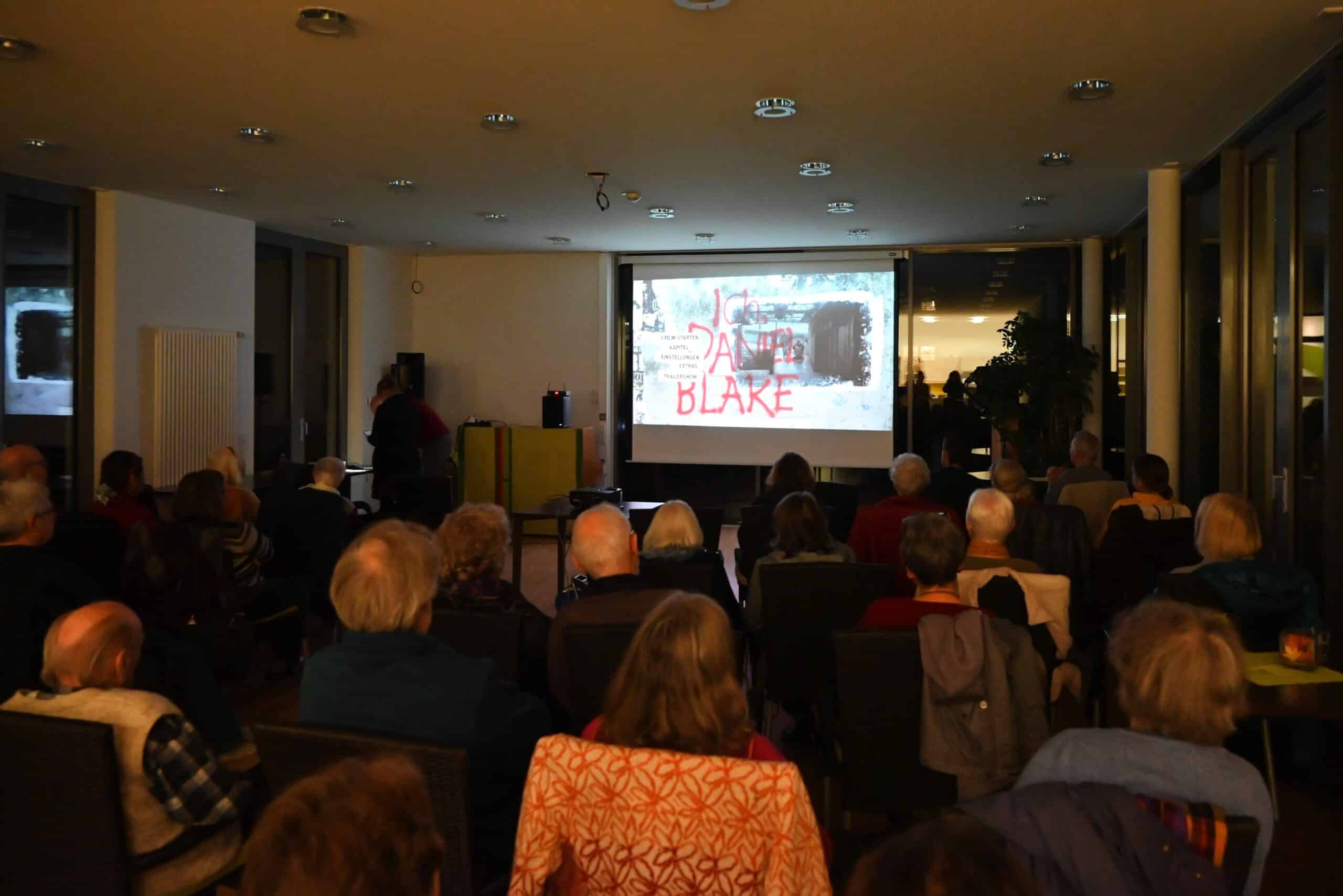 Eine Menge an Menschen sitzt in einem dunklen Veranstaltungsraum und schaut den Film Ich, Daniel Blake.
