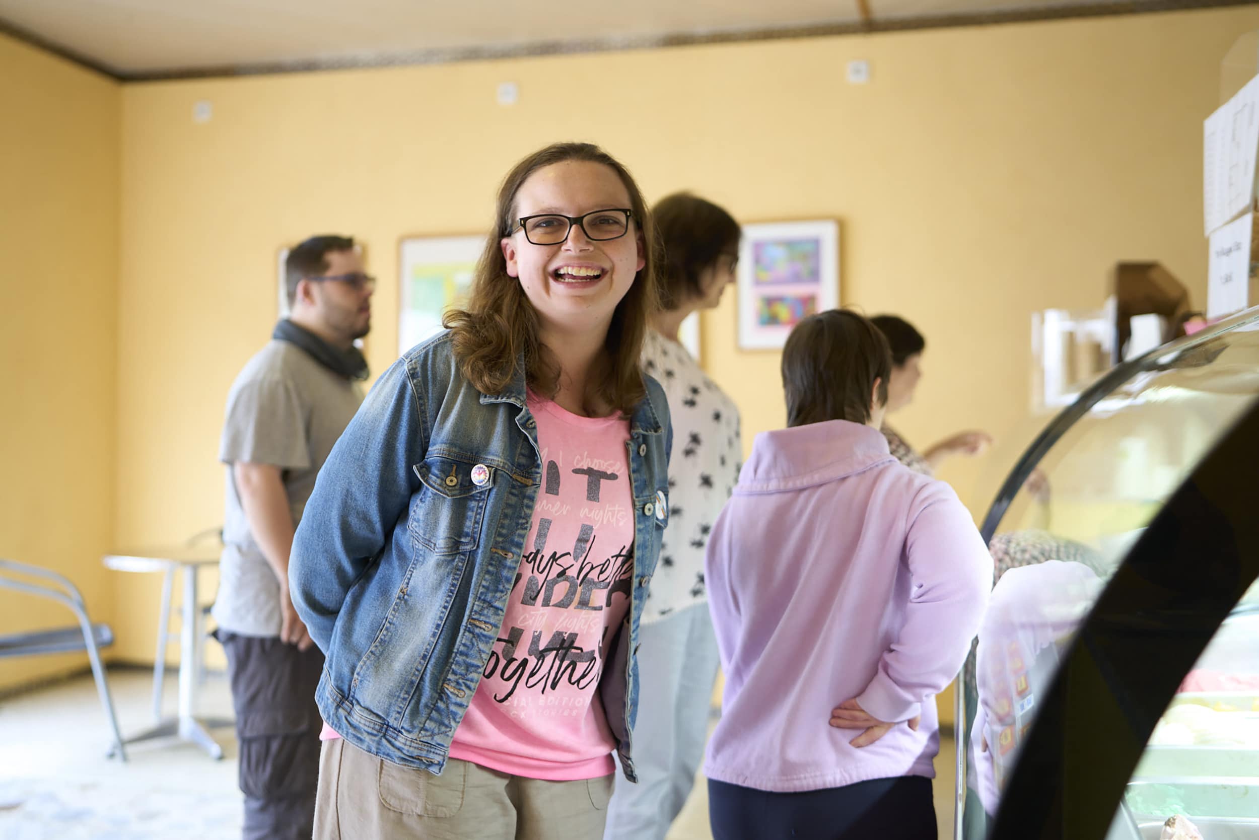 Vier Personen stehen vor einer Eis-Vitrine. Eine Frau schaut in die Kamera und lacht.