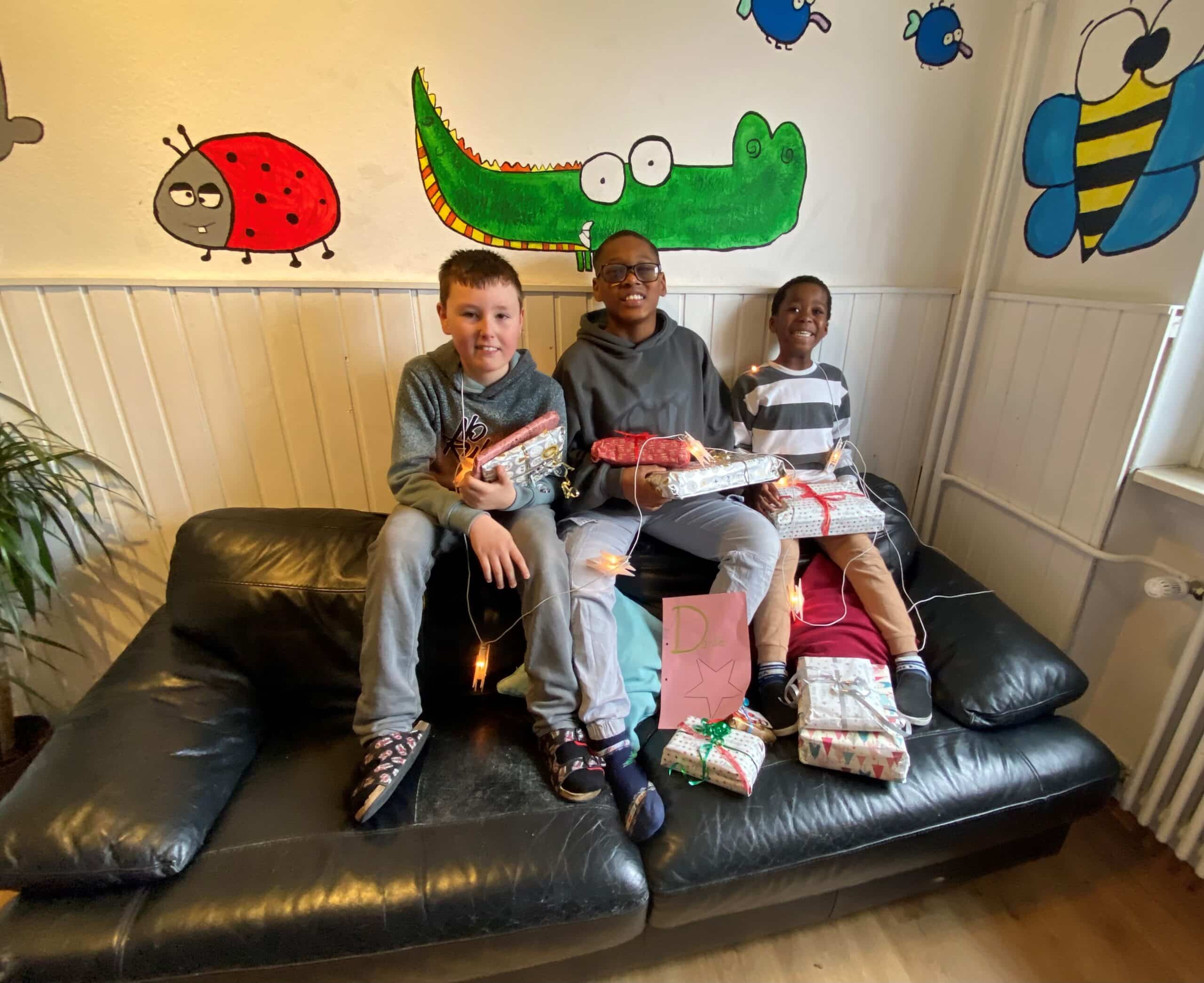 Drei Jungen sitzen auf einem Sofa. Sie halten Weihnachtsgeschenke in den Händen und lachen.