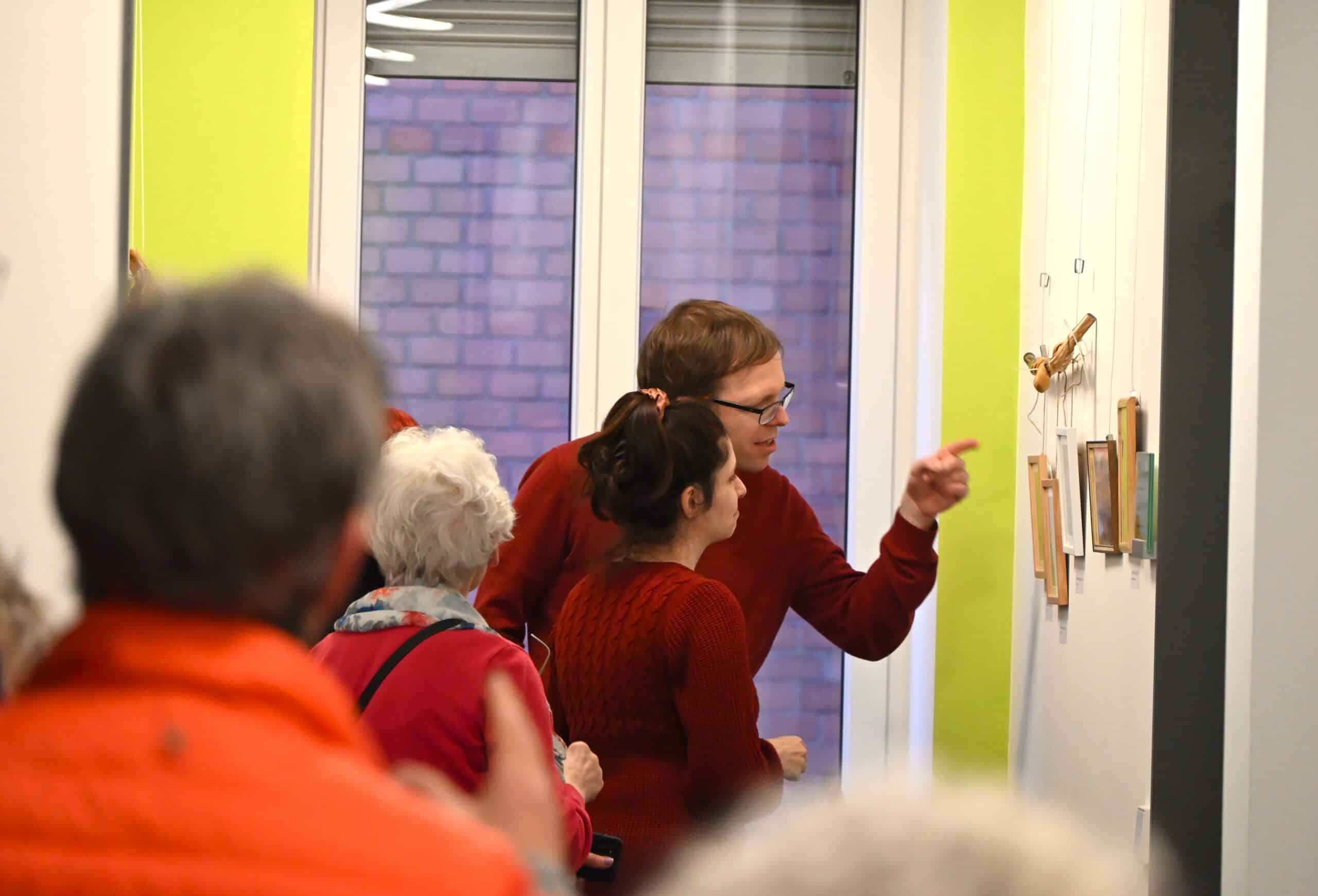 Ein Paar steht vor den Kunstwerken von Helga Betsarkis und unterhält sich über sie.