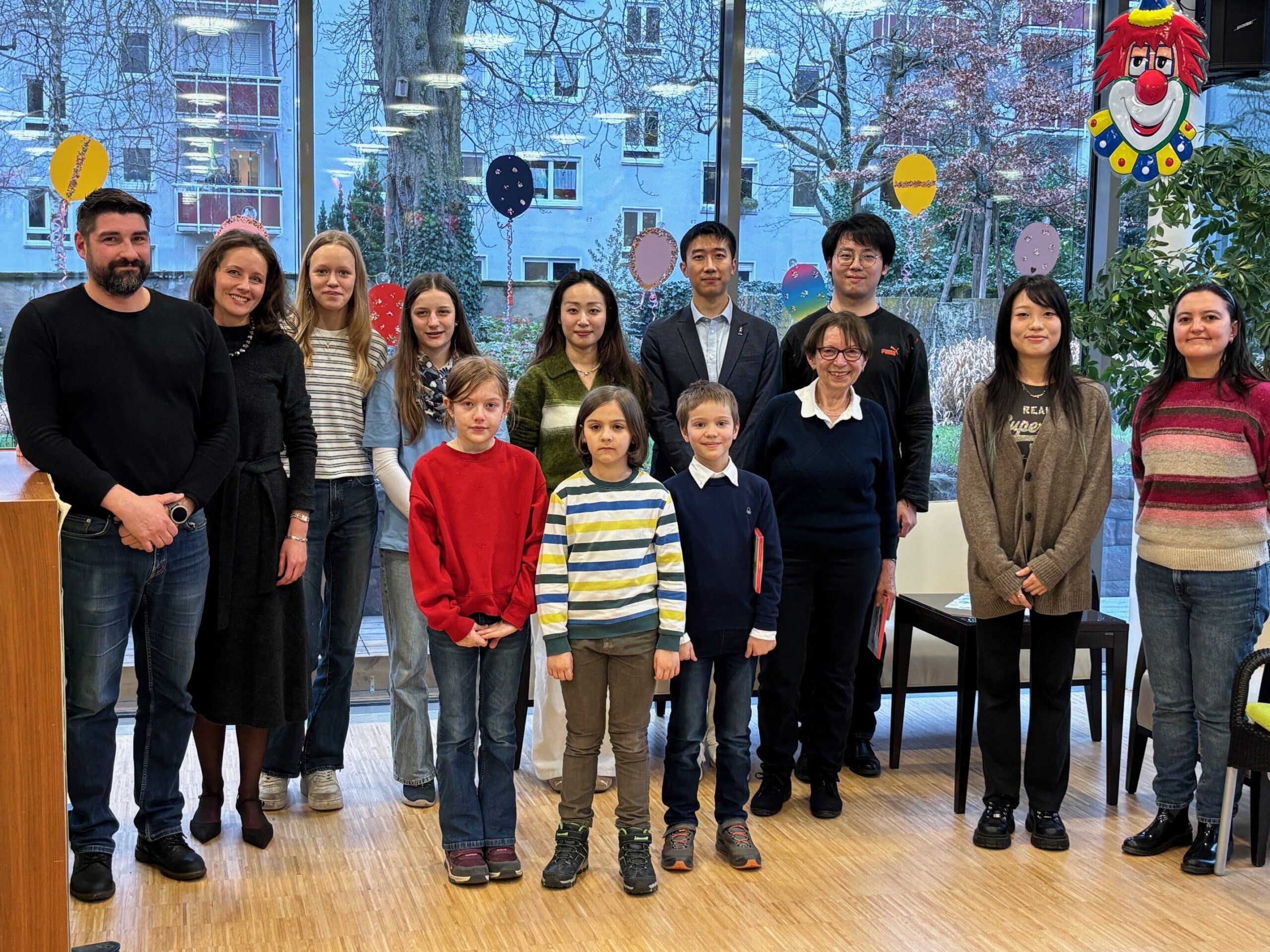 Eine Gruppe Menschen steht neben einem Klavier und lächelt in die Kamera. Vorne stehen drei Kinder.