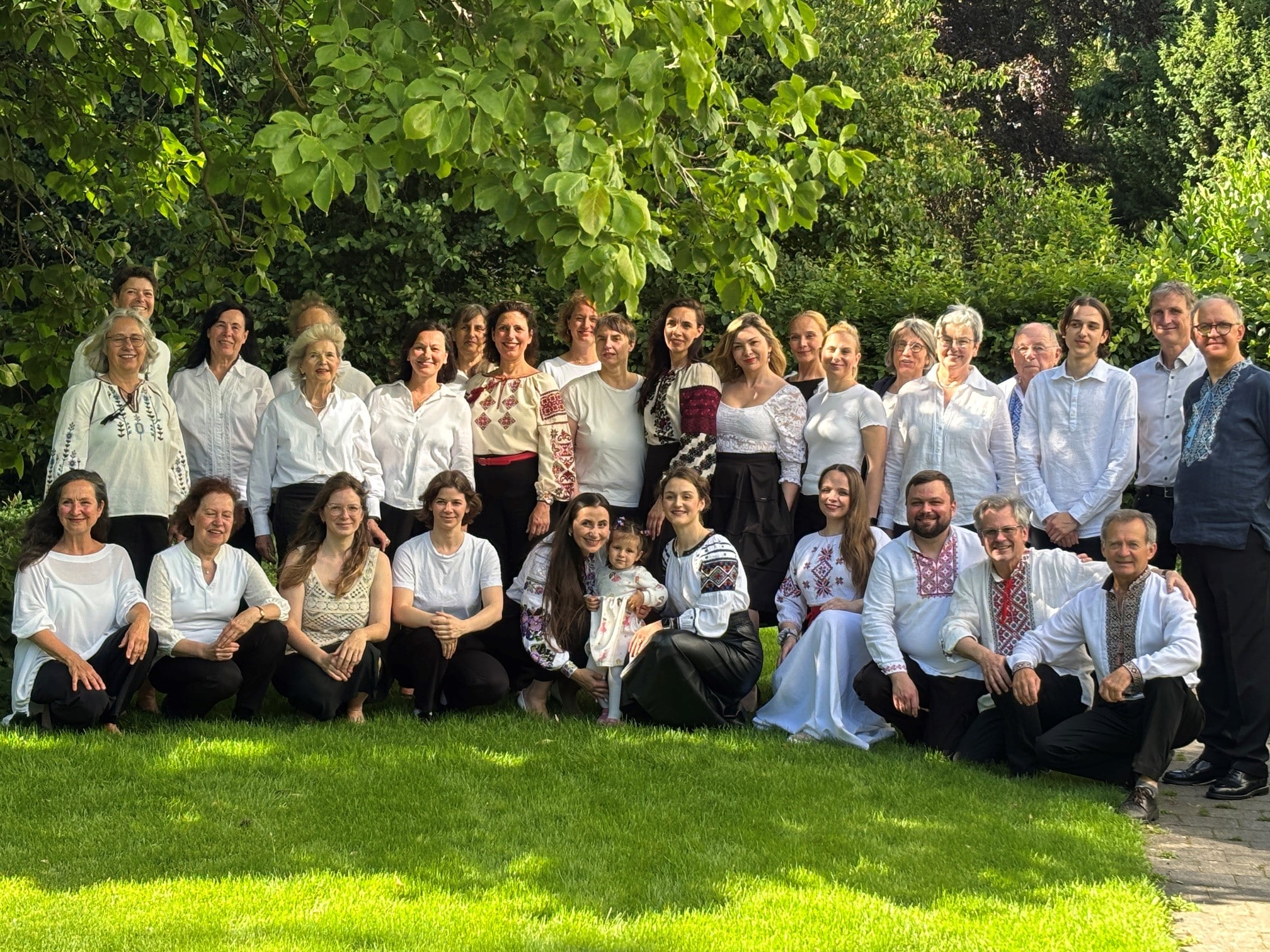 Die Mitglieder des Fächerchors und der Chorleiter stehen im Grünen, tragen weiße Oberteile und lächeln gemeinsam für das Gruppenbild in die Kamera.