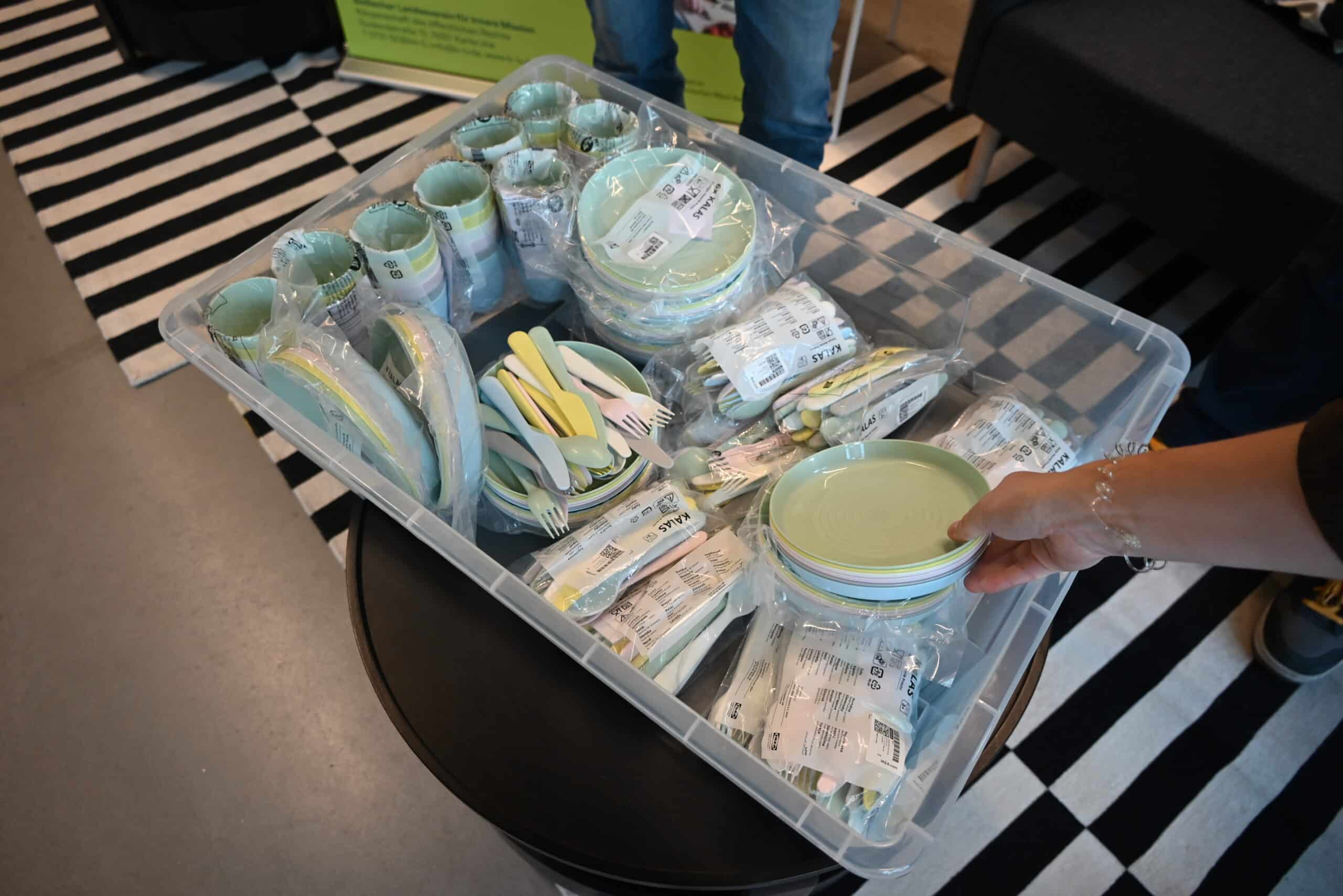 Eine Hand greift nach den Bechern aus einer Kiste von IKEA voller Plastikgeschirr.
