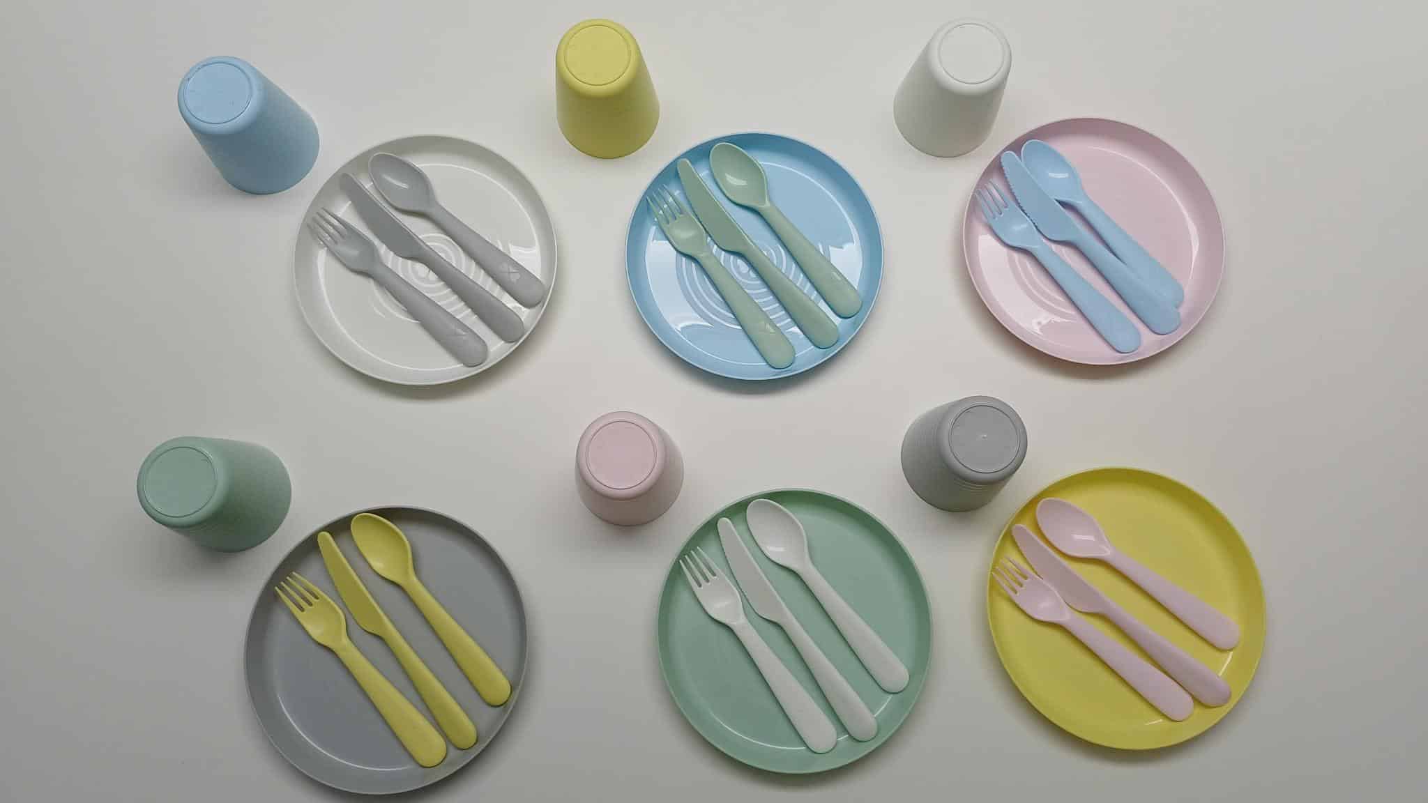 Das bunte IKEA Plastikgeschirr ist zurecht gelegt mit Tellern, Besteck und Bechern in den Farben gelb, mintgrün, hellblau, grau und rosa.