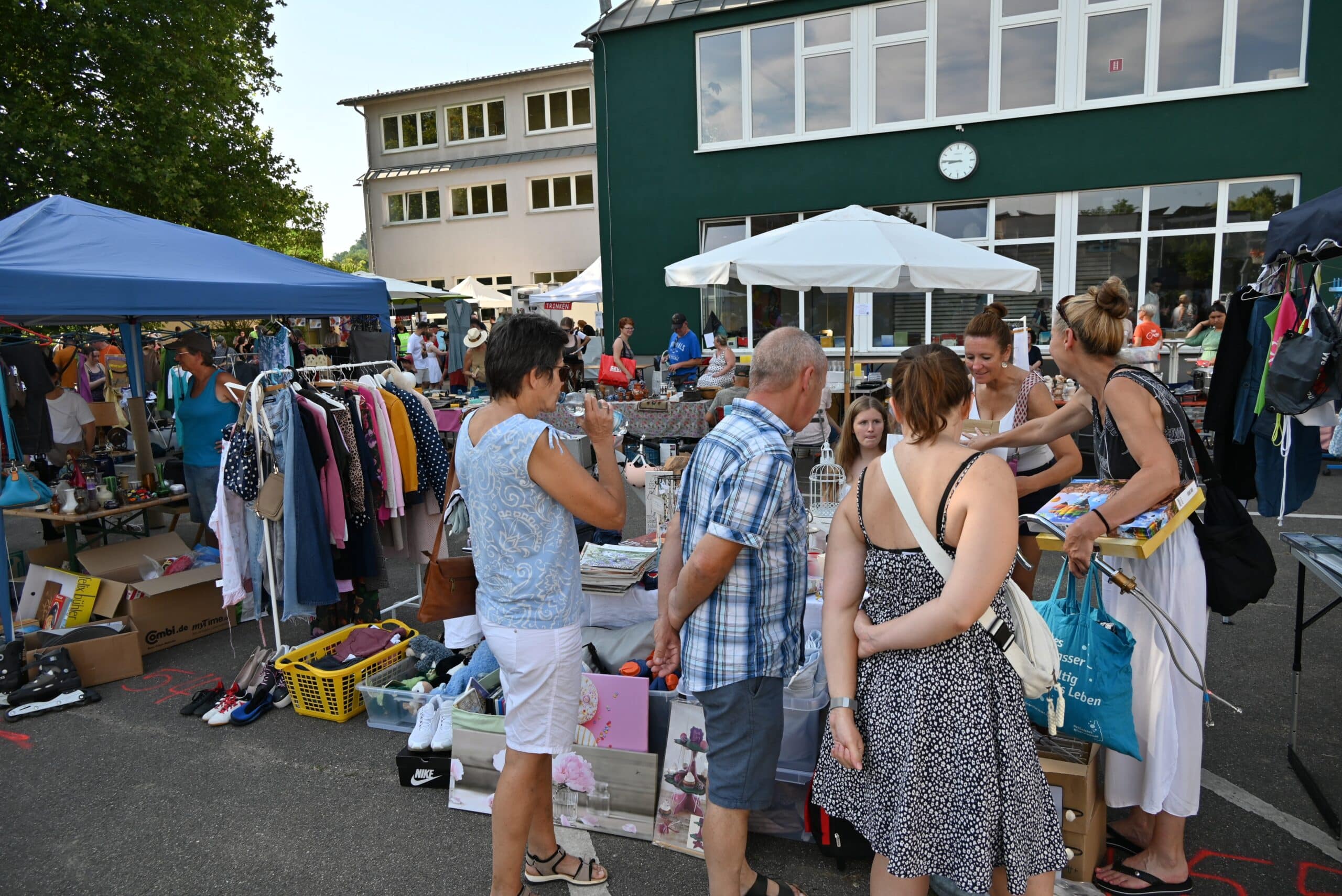 Drei Frauen und ein Mann stöbern an einem Stand im Schatten
