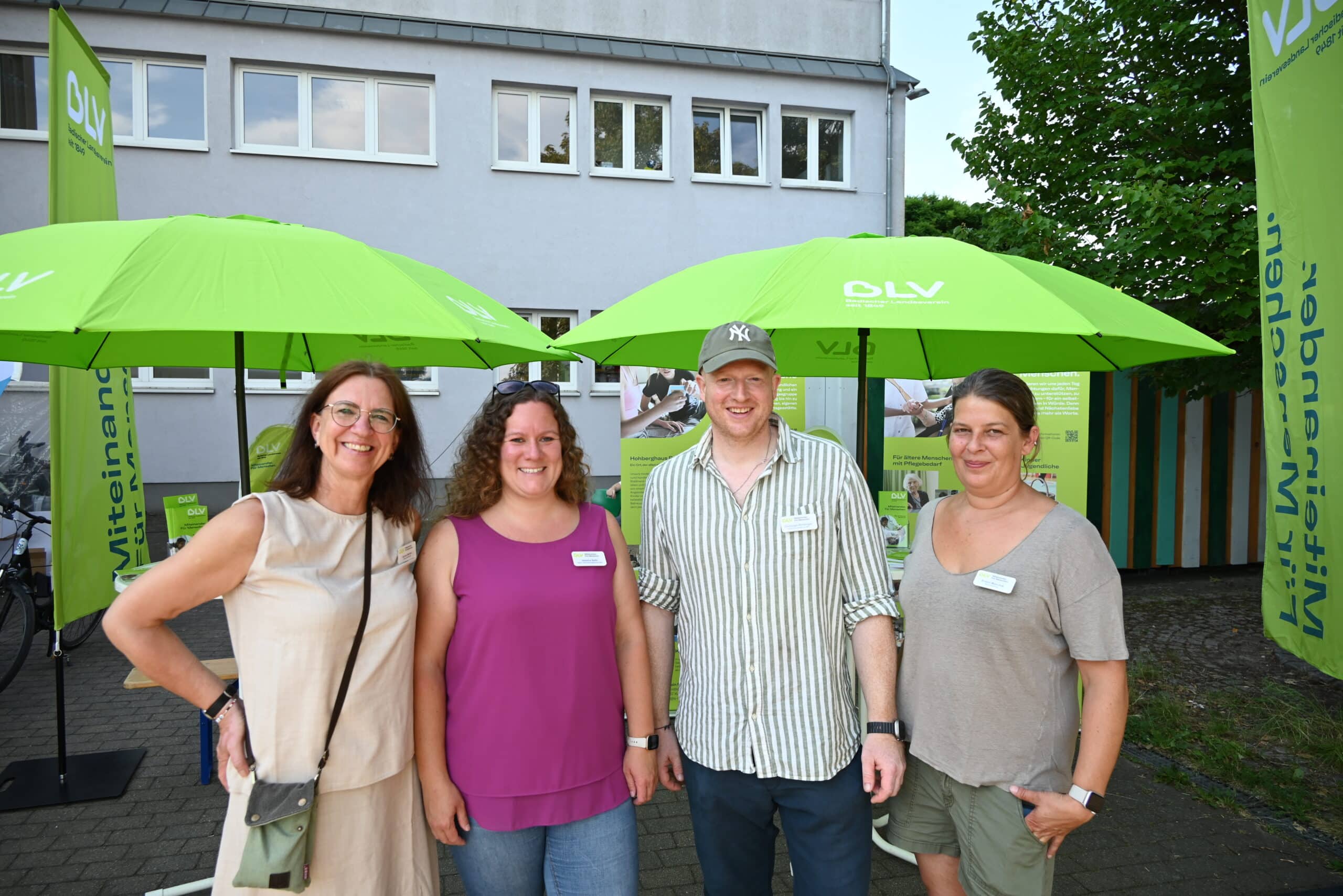 Drei Frauen und ein Mann lächeln in die Kamera, im Hintergrund der BLV-Infostand mit grünen Sonnenschirmen und Fahnen.