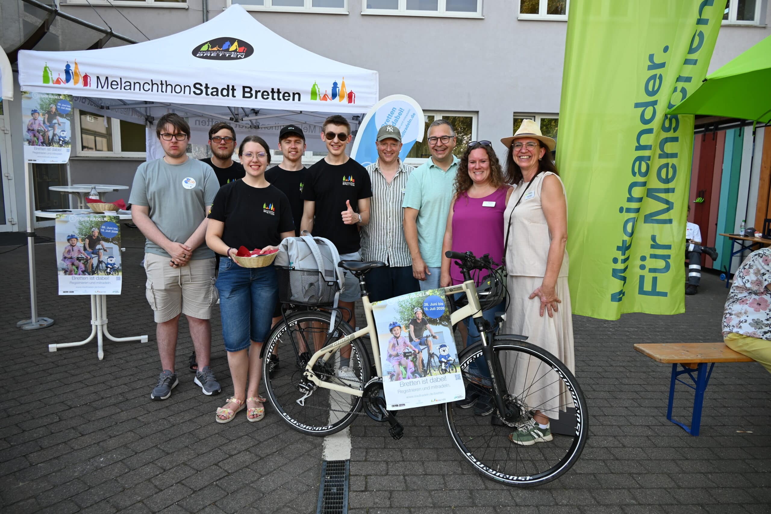 Neun Personen lächeln in die Kamera, rechts die Fahnen des BLV, dahinter das Zelt der Stadt Bretten und im Vordergrund das Fahrrad mit Werbung zur Aktion Stadtradeln.