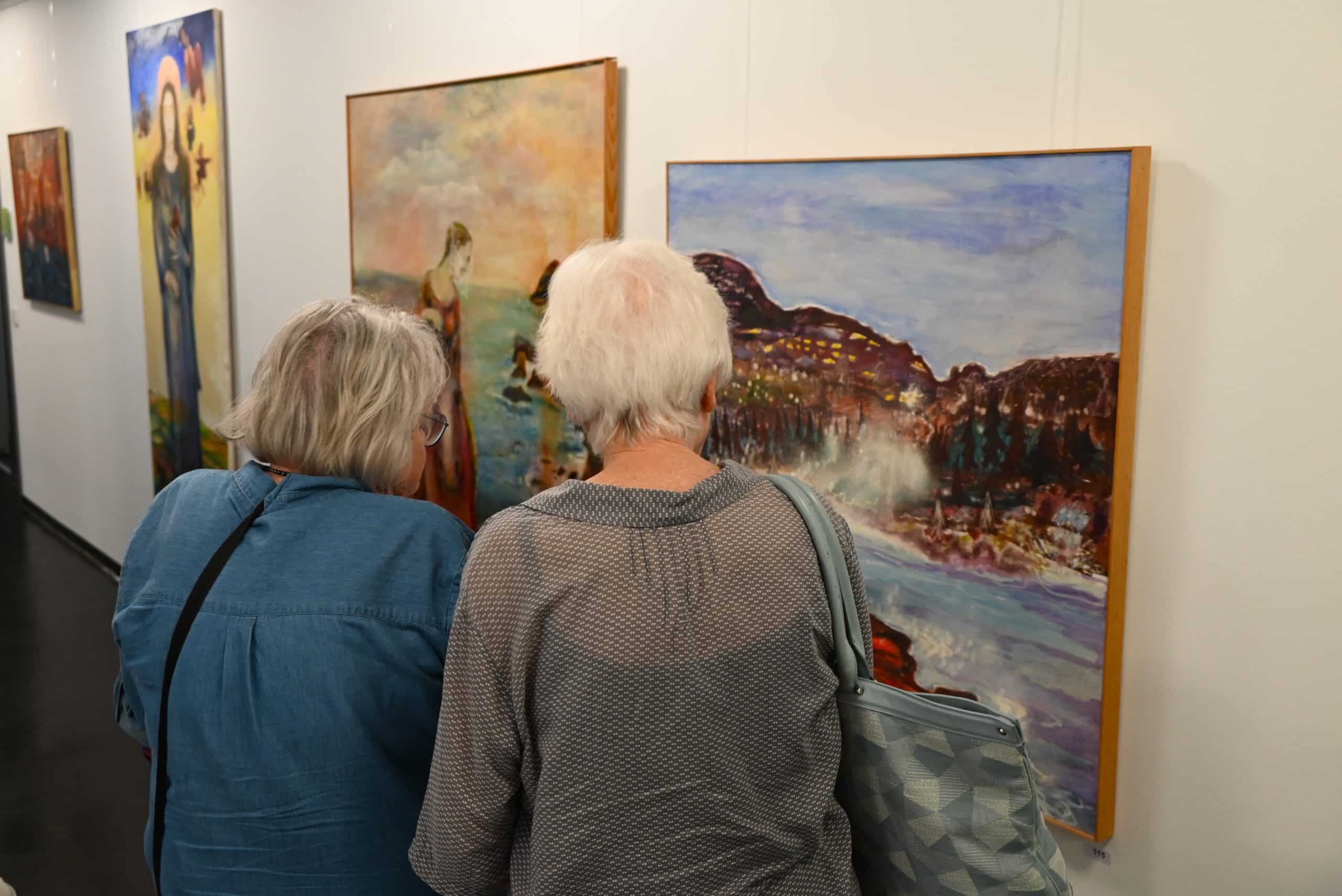Zwei Frauen mit grauen Haaren betrachten die Bilder der Ausstellung