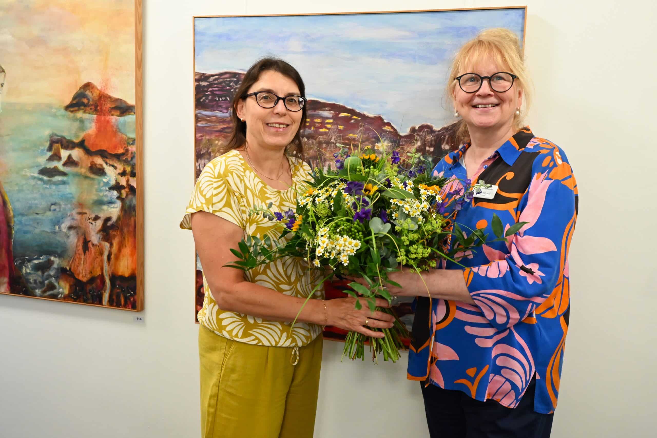 Bettina Duschl und Christine Jung-Weyand halten einen Blumenstrauß in den Händen und lächeln in die Kamera.